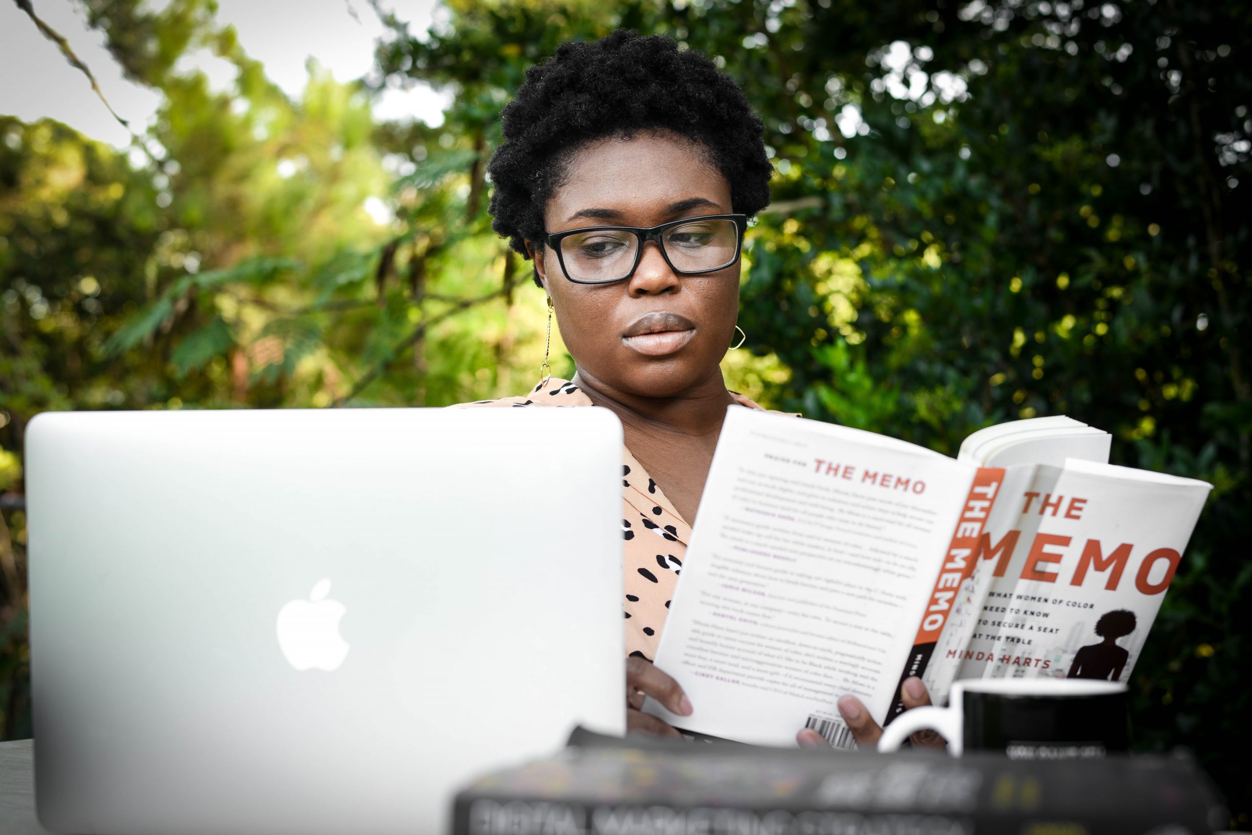 Woman in glasses reading the book by the laptop